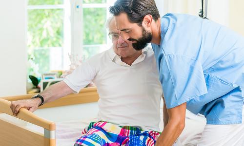 Pfleger hilft altem Herren aus dem Bett